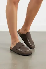 Zueco de gamuza marrón con costuras blancas decorativas en la puntera, tira en el empeine tipo mocasín y suela de corcho con base de goma.