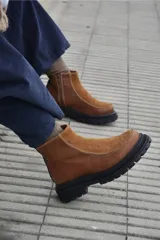 Bota corta de cuero color marrón con paneles en gamuza al tono, diseño de punta redondeada y suela track negra de goma. Presenta cierre lateral y detalle de costuras a la vista.