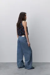 Jean negro de tiro alto y pierna wide leg, confeccionado en denim de caída firme con diseño de cinco bolsillos, pasacintos, cierre frontal con botón y ruedo desflecado.