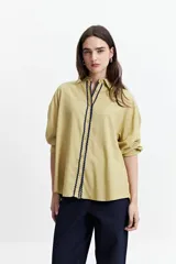 Camisa oversize color crema con detalles de puntilla roja en el frente.