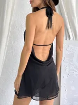 Vestido corto negro con escote halter y cuello drapeado. Presenta un diseño ajustado en la parte superior y falda con volados en la parte inferior.