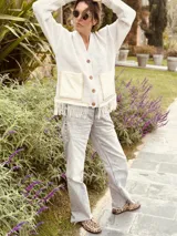 Cardigan de punto color beige con escote en V, cierre frontal con botones, bolsillos delanteros aplicados y detalle de flecos en el ruedo.