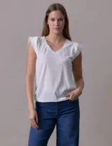 Remera blanca de modal, marca French Laundry, con escote en V. Presenta apliques de puntilla en las mangas y el escote, y un detalle fruncido en los hombros.