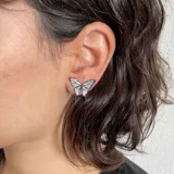 Par de aros tipo botón con forma de mariposa plateada con detalles en negro.