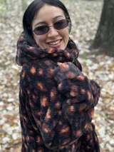 Buzo color beige de poliéster con textura de piel de oso, capucha con cuello alto, mangas largas y bolsillo tipo canguro.