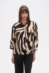 Camisa de corte holgado con estampado animal print tipo cebra en tonos negro y beige. Presenta cuello mao, cierre frontal con botones y un bolsillo aplicado en el pecho.