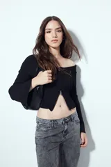 Top de punto acanalado negro, con diseño off-shoulder y escote amplio. Presenta mangas largas y cierre frontal completo con doble cursor, permitiendo ajustar la apertura superior e inferior.