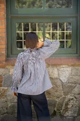 Blusa de algodón con estampado vichy en blanco y negro. Presenta un diseño con frunces en la parte superior del pecho, cuello alto con volado y mangas largas amplias con puños elásticos.