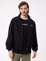 Campera Rusty de corte clásico, color negro, con cierre frontal completo, cuello alto y puños elásticos. Presenta un diseño minimalista con el logo de la marca bordado en el pecho.