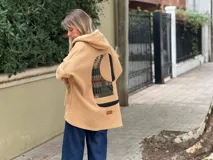 Campera tipo hoodie de corderito color camel, con diseño de collage abstracto en la espalda que combina texturas y estampados geométricos. Posee capucha y corte holgado.