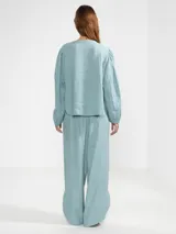 Cardigan abotonado color celeste, confeccionado en lino 100% italiano, con silueta relajada, dobladillo curvado, puños elásticos y un charm floral en el primer botón.