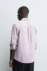 Camisa de corte regular fit confeccionada en tejido de algodón con textura. Presenta cuello solapa, cierre frontal de botones, manga larga con puños abotonados y un bolsillo plastrón en el pecho.