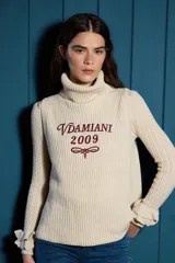 Chaleco de tejido de punto color crema con cuello alto y bordado frontal en color bordó con la inscripción Vdamiani 2009. Presenta detalles de volados en las sisas.