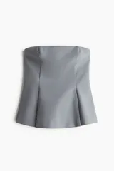 Top tipo bustier color gris, sin mangas y sin tirantes, con corte entallado en el pecho y acampanado en el bajo gracias a pliegues tableados.