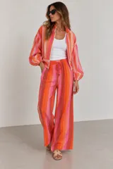 Pantalón de tiro alto y pierna ancha con estampado de rayas verticales en tonos rosados, naranjas y marrones. Cuenta con cintura elástica con cordón de ajuste y bolsillos laterales.
