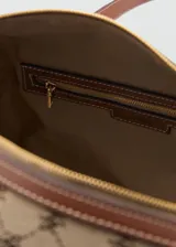 Bolso tipo bowling de diseño estructurado, confeccionado en tejido con estampado de monograma en tonos beige y marrón. Presenta detalles en cuero sintético marrón en las asas, esquinas y parches de sujeción, con herrajes metálicos dorados.