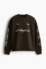 Buzo verde militar de corte oversized, confeccionado en mezcla de algodón con cuello redondo, puños y dobladillo acanalados. Cuenta con estampados en el frente, la espalda y las mangas, incluyendo inscripciones y estrellas.