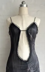 Vestido corto ajustado color negro con estampado a cuadros difuminado. Presenta escote pronunciado con abertura central y bordes de encaje negro. Tiene tirantes finos y frunces en la falda.