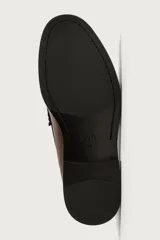 Mocasín de vestir color marrón oscuro, confeccionado en cuero, con detalle de antifaz y borlas decorativas en el empeine. Presenta una horma redonda y suela plana a tono.