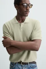 Polo de manga corta color verde azulado oscuro, confeccionado en tejido de punto con textura. Presenta cuello solapa y cierre frontal de botonadura.