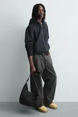 Bolso de hombro tipo hobo o media luna, confeccionado en tejido técnico negro. Presenta un bolsillo frontal con cierre y una correa ajustable para llevar al hombro.