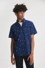 Camisa de manga corta color azul con estampado de pájaros blancos, cuello clásico con botones y bolsillo frontal con etiqueta roja.