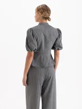 Chaqueta gris con diseño de rayas verticales y sutiles lentejuelas. Presenta cuello mao con lazo de gamuza, botones decorativos en forma de flor, recorte en la cintura y mangas abullonadas con puño elástico.