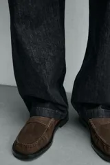 Mocasín de vestir para hombre, fabricado en piel con acabado serraje (gamuza) color marrón oscuro/café. Presenta un detalle de antifaz en el empeine con costuras visibles y horma cuadrada. La suela es negra y a contraste con un ligero tacón.