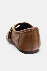 Zapato tipo bailarina de cuero color marrón, con punta redonda, detalle de pespuntes y perforaciones (picados) en el empeine. Presenta una tira con hebilla metálica dorada sobre el empeine.