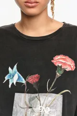 Remera negra de corte recto y holgado, confeccionada en algodón orgánico. Presenta cuello redondo, mangas cortas y estampa frontal de un ramo de flores en tonos coloridos con detalles artísticos.