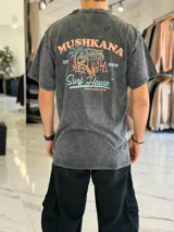 Remera oversize gris con efecto gastado, de manga corta, con estampa en la espalda de estilo surf con la inscripción "Mushkana Surf House".