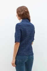 Camisa de manga corta en color bordó, confeccionada en tejido con textura de punto smock. Presenta cuello clásico, cierre frontal con botones y un ajuste entallado al cuerpo.