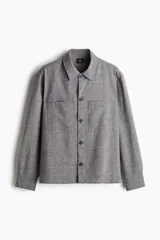 Sobrecamisa gris de tejido texturizado, con cuello inglés, tapeta lisa con botones oscuros y dos bolsillos superiores abiertos. Presenta un corte recto y holgado.
