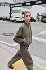 Cazadora estilo bomber color gris, con cuello subido, manga larga, bolsillos delanteros de vivo y cierre frontal con cremallera. Presenta bajo ajustable con cordones elásticos laterales.