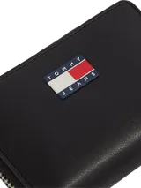 Billetera negra con cierre de cremallera, dos compartimentos principales y logo Tommy Jeans en el frente.