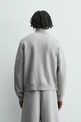 Chaqueta de punto compacto con mezcla de algodón, corte relajado, cuello subido, manga larga, bolsillos laterales de vivo y cierre frontal con cremallera.
