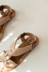 Sandalias chatitas de cuero en tono nude, con diseño de tiras cruzadas en el empeine y elástico en el talón para mayor ajuste. Presentan una plantilla acolchada y detalles en cuero charolado en la parte posterior.