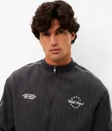 Campera deportiva de helanca color gris oscuro, con diseño de raya diplomática fina, cuello bomber, cierre frontal y bordados en el pecho.