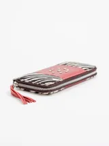 Billetera rectangular de cuero con cierre perimetral, diseño combinando laterales de pelo con estampado animal print tipo cebra y franja central roja con tachas metálicas dispuestas en forma circular. Cuenta con tirador de cierre en flecos de cuero rojo.