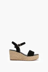 Sandalia de gamuza color negro con plataforma de yute trenzado, tira ancha en la parte delantera y tira ajustable al tobillo con hebilla metálica dorada.