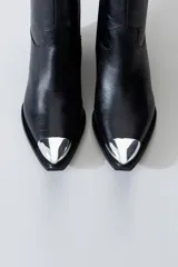Bota estilo texana de cuero negro con puntera metálica plateada, taco cuadrado y cierre lateral interno.