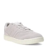 Championes urbanos New Balance de estilo retro, confeccionados en gamuza color gris claro con detalles en material sintético. Presentan el logo N característico en los laterales, cierre mediante cordones y suela de goma en tono crema.