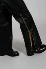 Pantalón negro de cuero con corte recto y abertura lateral en el tobillo, decorada con pespuntes en hilo amarillo/dorado en zigzag.