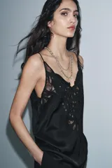 Top negro de viscosa con escote pico y tirantes finos. Presenta un aplique de encaje negro con diseño ornamental en el centro del pecho.