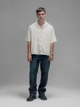 Camisa de manga corta color blanco roto, con cuello clásico y cierre frontal de botones.