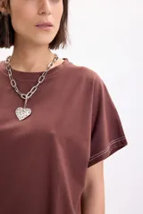 Camiseta marrón de manga corta holgada, con cuello redondo y costuras con pespuntes en color blanco contrastante en el dobladillo y las mangas.