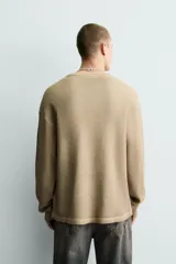 Sudadera de corte relajado confeccionada en tejido con textura waffle, color beige con efecto lavado. Presenta cuello redondo, manga larga con franjas laterales oscuras y estampado frontal con texto y número en contraste.