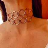 Gargantilla doble estilo choker, compuesta por dos tiras de símil gamuza que sostienen una serie de argollas metálicas plateadas entrelazadas.