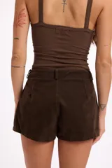 Short de efecto gamuza en color marrón oscuro, con detalle de tachas metálicas en el borde inferior y bolsillos, incluye cinturón a tono con hebilla.