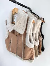 Chaleco estilo gamulán con interior y bordes de piel sintética. Presenta cierre frontal metálico, bolsillos laterales con cierre y detalles de costuras visibles.